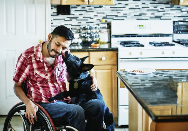 Lachende man in rolstoel laat gezicht likken door hond terwijl hij in keuken rondhangt