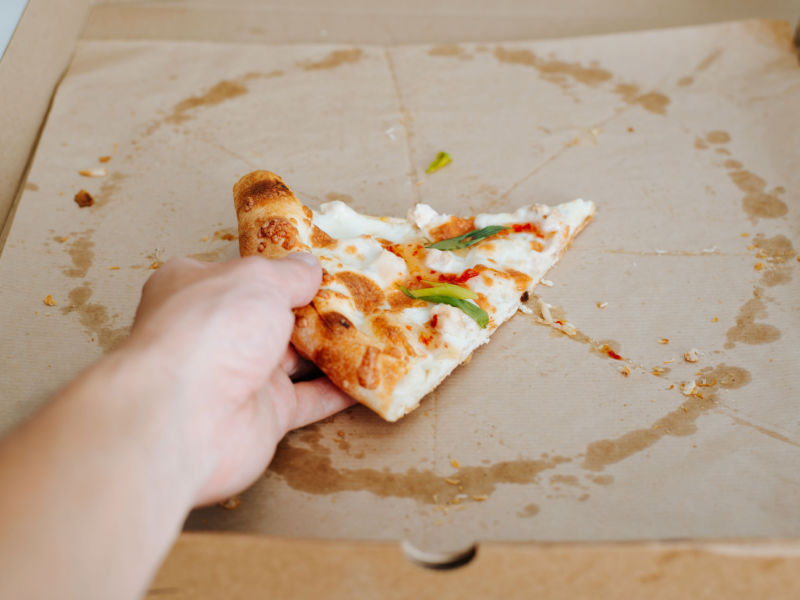 handgreep voor laatste stuk pizza in pizzadoos met vetvlekken