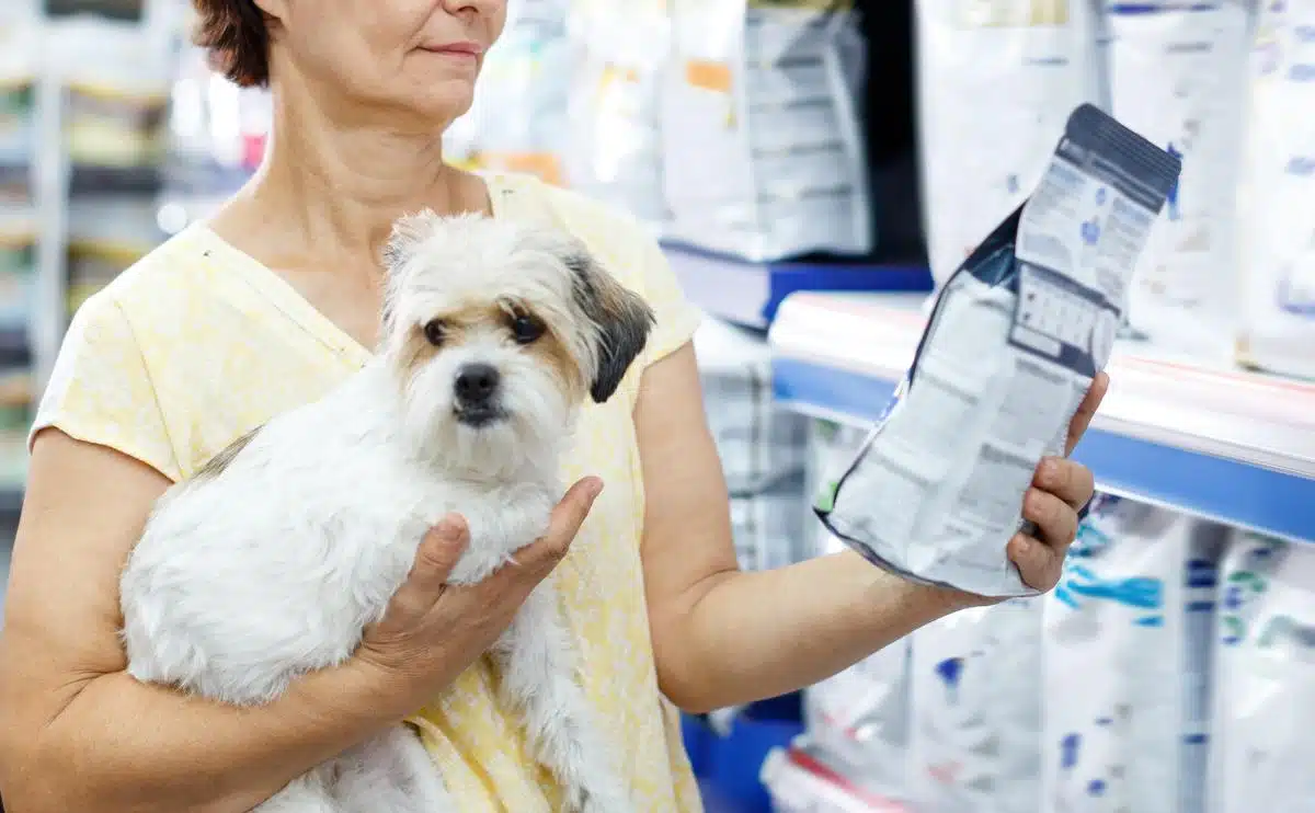 vrouw die kijkt naar hondenvoerzak in dierenwinkel met hond in andere arm