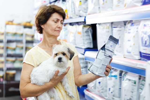 Vrouw en hond die voor voedsel voor huisdieren winkelen